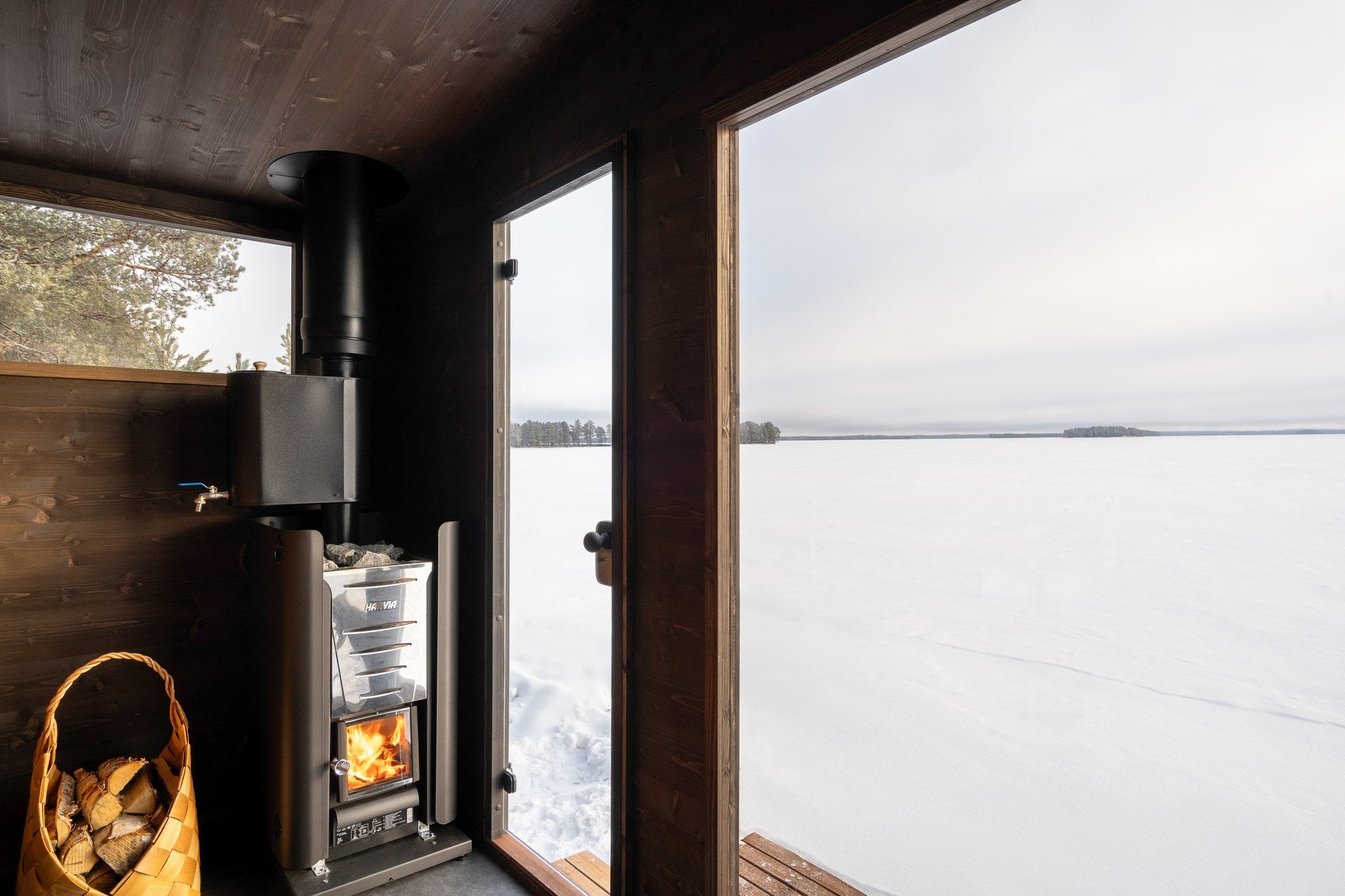 Vedkamin med vedkorg och fönster i basturummet i Lapelland Large